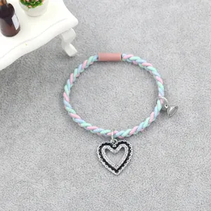 Close-up of a colorful woven bracelet featuring a rhinestone heart pendant and silver bell