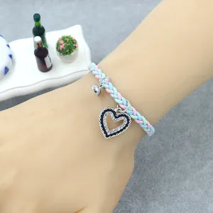Handmade woven friendship bracelet with heart pendant and bell charm on a model