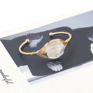 Detail van een ruw wit kristal omwikkeld met gouddraad op een C-vormige open armband
