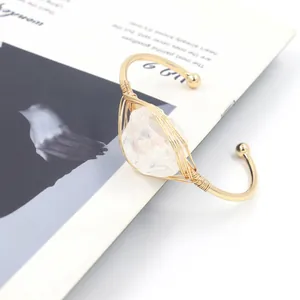 Detail van een ruwe witte kristal omwikkeld met gouden draad op een C-vormige armband