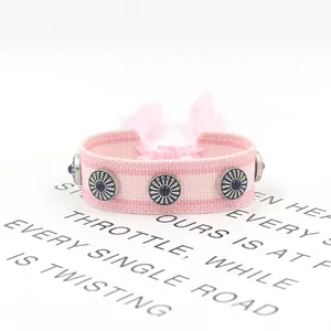 Detalle de pulsera tejida rosa con tachuelas de cuentas azules y borlas ajustables