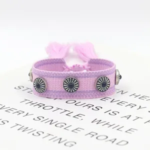 Detalle de la pulsera tejida boho púrpura con tachuelas de girasol y borlas rosas