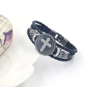 Detail of multi-layer leather bracelet featuring a vintage metal cross charm and woven cords
