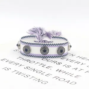 Detalle de pulsera tejida bohemia con borlas moradas y tachuelas de girasol de metal