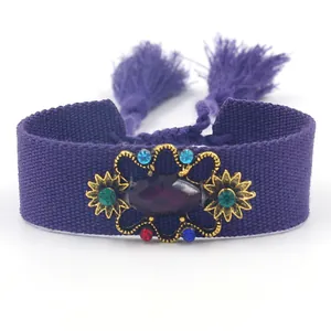 Pulsera étnica tejida morada con borlas, pedrería colorida y base floral dorada