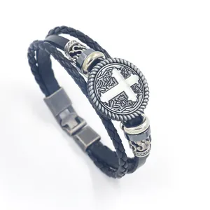 Detail of multi-layer leather bracelet featuring woven straps and antique silver cross charm
