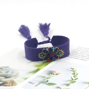 Detalle de pulsera boho tejida morada con pieza central dorada y pedrería de colores