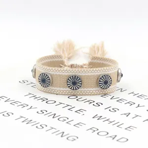 Detalle de pulsera boho tejida con remaches plateados y cuenta azul en tarjeta blanca