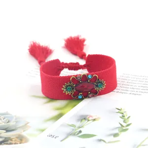 Detalle de pulsera tejida roja con gema dorada vintage y borlas rojas étnicas