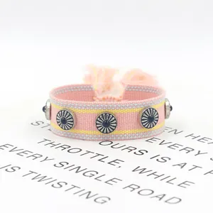 Detalle de pulsera tejida rosa con borlas, tachuelas plateadas y diseños étnicos