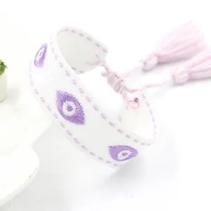 Detail van geweven wit evil eye armband met paars borduursel en kwastjes
