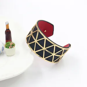 Detail of wide gold hollowed cuff bracelet featuring red inner lining and geometric pattern