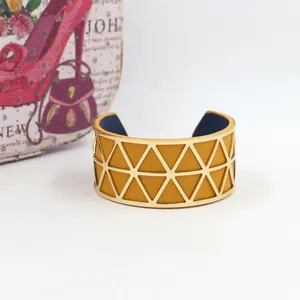 Detail of hollow geometric gold metal cuff bracelet with mustard and navy leather lining