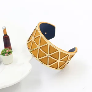 Detail of wide golden geometric metal bangle with dual-color yellow and navy leather inlay