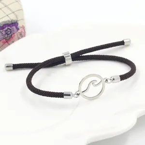 Detail van een verstelbare donkerbruine gevlochten armband met zilveren golfbedel