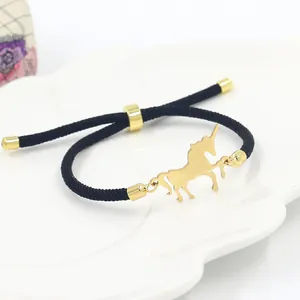 Minimalist gold unicorn charm bracelet with adjustable black braided rope on a plate