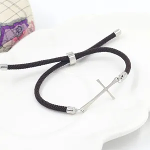 Détail de la croix sur bracelet tressé marron avec nœud coulissant réglable