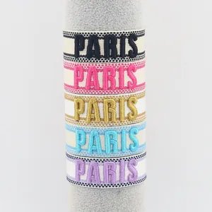 Detail of colorful woven friendship bracelets with 3D PARIS embroidery on gray velvet display
