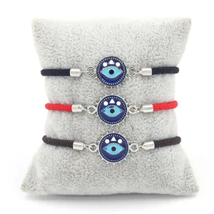 Σετ τριών υφαντών βραχιολιών Evil Eye σε μαύρο, κόκκινο και καφέ πάνω σε γκρι μαξιλάρι