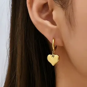 Golden heart pendant earrings worn on ear showing polished metal finish and elegant design
