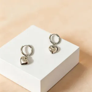 Elegant silver heart pendant hoop earrings displayed on a minimalist white pedestal