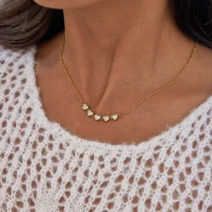 Detailed macro view of a gold heart pendant necklace with clear zircons on a model
