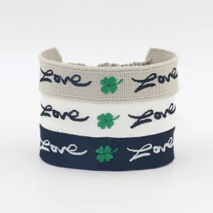 Tre braccialetti intrecciati Love trifoglio ricamati in blu, bianco e grigio con nappine