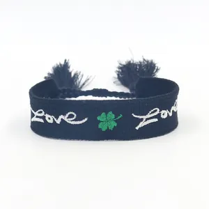 Dettaglio di bracciale intrecciato nero con quadrifoglio verde e ricamo Love