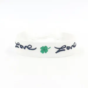 Dettaglio macro del bracciale in tessuto bianco con quadrifoglio verde e ricamo Love