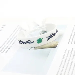 Dettaglio del bracciale intrecciato bianco con ricamo Love, quadrifoglio e nappe morbide