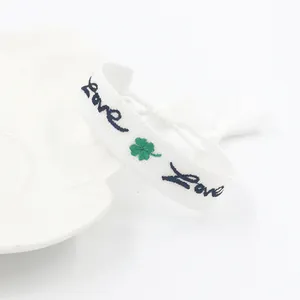 Bracciale intrecciato bianco con ricamo Love, quadrifoglio verde e nappe eleganti