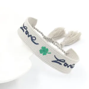 Bracciale quadrifoglio ricamato grigio chiaro con scritta Love e nappe su base bianca
