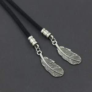 Vintage Bolo Tie met zwart gevlochten koord en zilveren veerhangers op grijze achtergrond