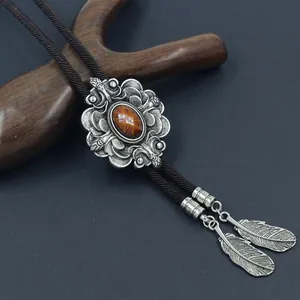 Detail einer silbernen Bolo-Krawatte mit braunem Edelstein und Federanhängern
