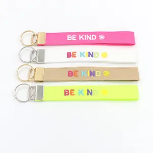 Detalle de cuatro llaveros bordados BE KIND de colores con herrajes metálicos