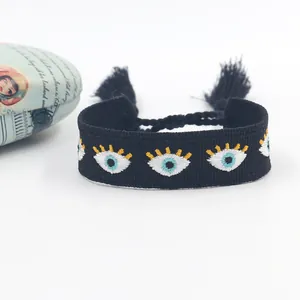 Macro detail of bohemian black woven wristband featuring evil eye embroidery and tassels