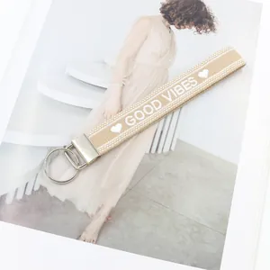 Detalle del llavero de tela caqui con texto GOOD VIBES blanco y anillo de metal plateado