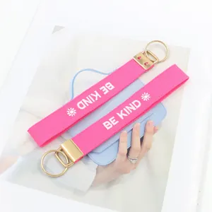 Detalle del llavero rosa bordado BE KIND con anilla dorada sobre un bolso azulado