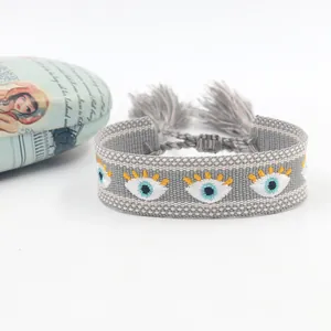 Macro detail of bohemian grey woven wristband featuring embroidered evil eye and tassels