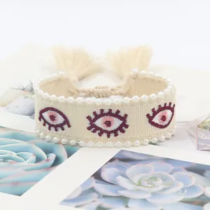 Detail of bohemian woven bracelet with embroidered evil eye patterns and pearl beads
