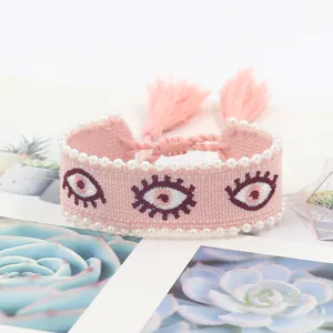 Pink woven evil eye bracelet with white faux pearls and tassel charms on a floral card