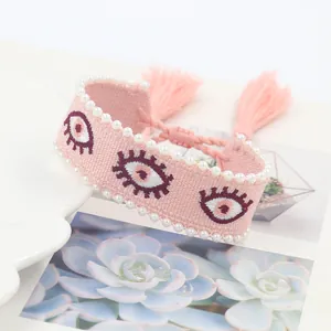 Detailed embroidery of evil eye on pink woven pearl bracelet with stylish tassels