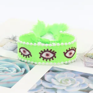 Detail view of woven evil eye bracelet with white faux pearls and vibrant tassels