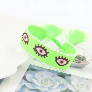 Detail of neon green woven bracelet with embroidered evil eyes and pearl beads trim