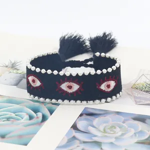 Close-up of woven evil eye bracelet with white pearl trim and black fringe tassels