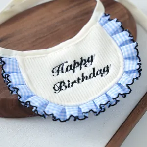 Detailed view of white knit pet bib with blue gingham trim and Happy Birthday embroidery