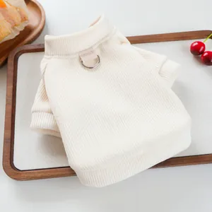 Off-white knit pet sweater with leash D-ring shown on a wooden tray with accessories