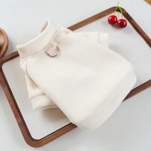 Detail of off-white knitted pet vest showing ribbed texture and metal D-ring attachment