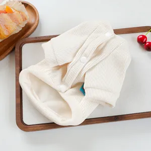 Detail of cream rib-knit pet cardigan with white buttons on a rustic wooden tray