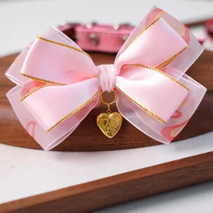 Gros plan d'un collier à nœud en satin rose avec pendentif coeur doré pour animaux